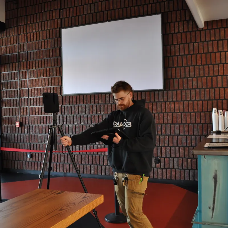 Man adjusting camera on tripod in a modern room with brick walls and large windows during daytime