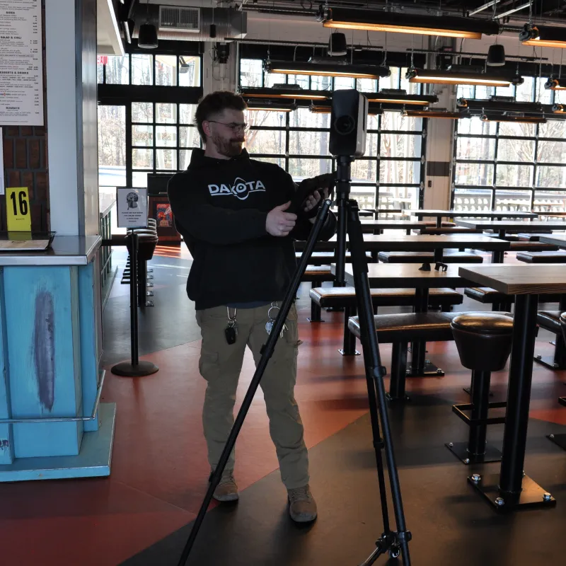 Man adjusting a tripod-mounted camera inside a modern empty restaurant with large windows and blue counter.