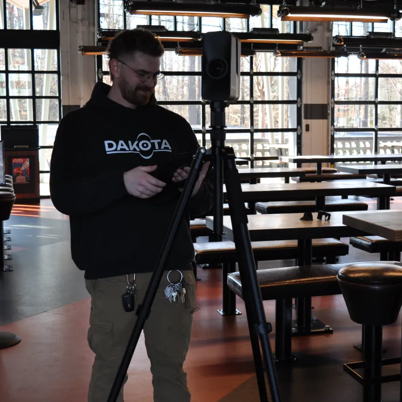 Man adjusting camera on tripod inside empty restaurant with natural light from windows