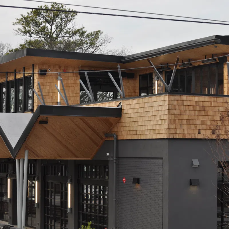 Modern two-story building with wood siding and large windows housing Grindhouse restaurant.