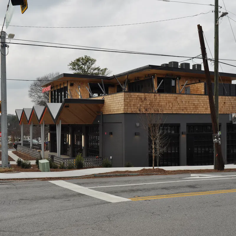 Modern two-story building with wooden accents and large windows on a cloudy day at a street corner.