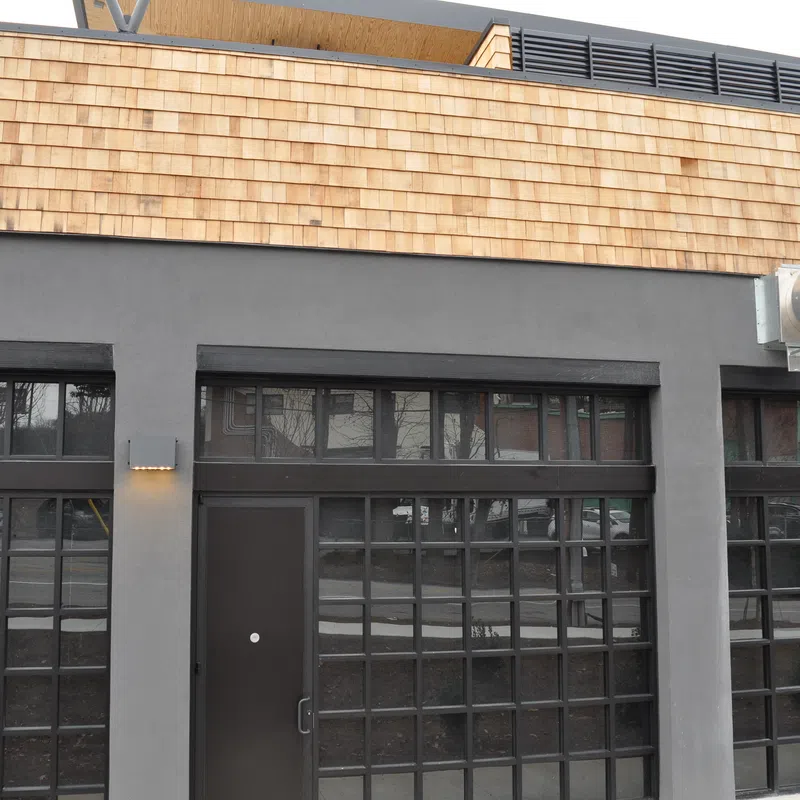 Modern commercial building facade with large grid windows, dark door, gray stucco, and wooden shingle trim.