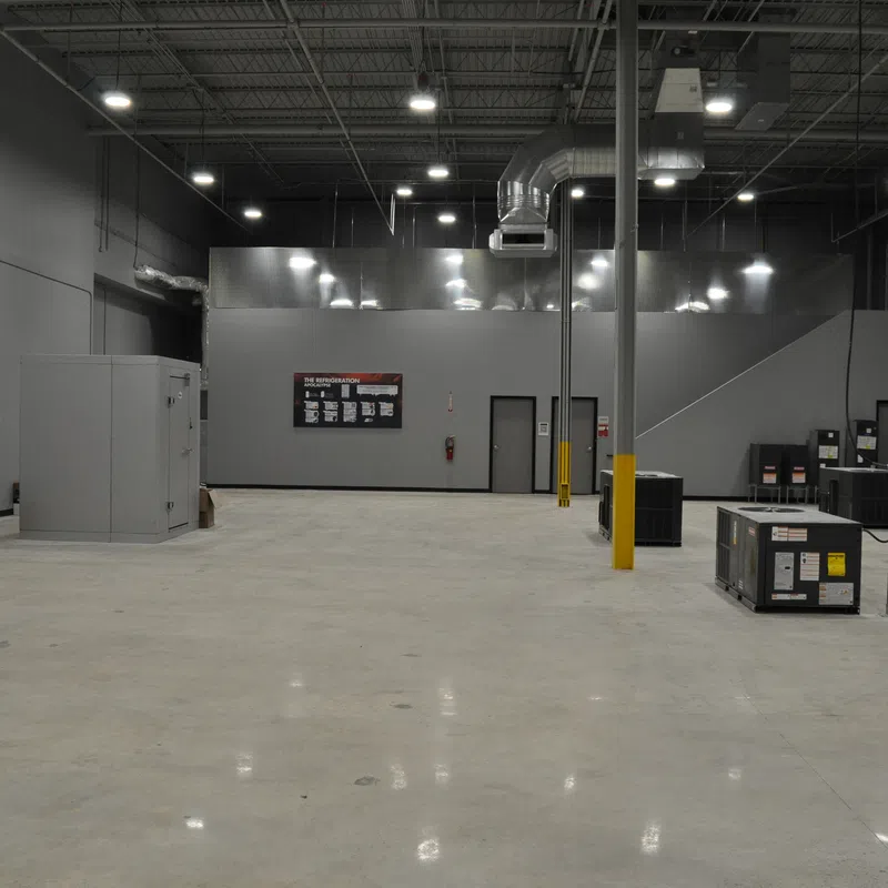 Large empty industrial warehouse space with gray walls, concrete floor, and scattered HVAC units under bright ceiling lights