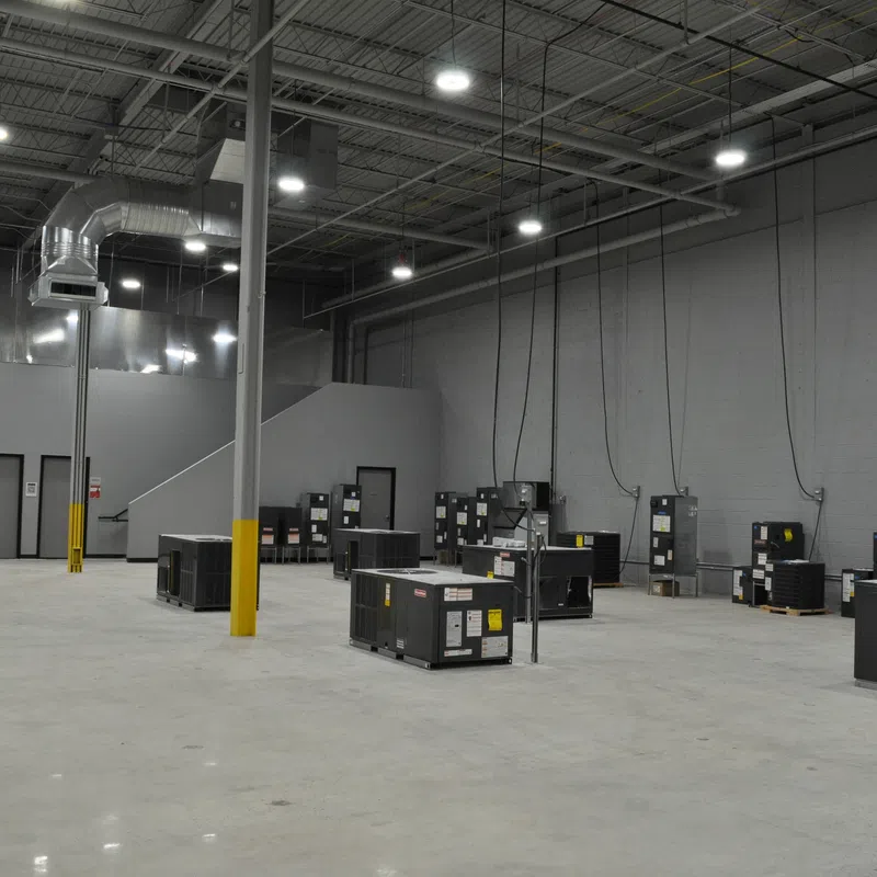 Spacious industrial warehouse with HVAC units installed on concrete floor and high ceiling lighting.