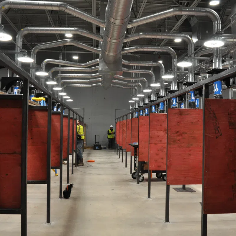 Industrial welding booths with ventilation pipes in a spacious workshop under bright lighting.