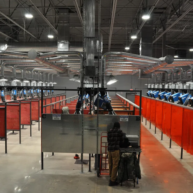 Industrial welding workshop with multiple welding stations separated by orange safety screens and equipped with blue welding machines.