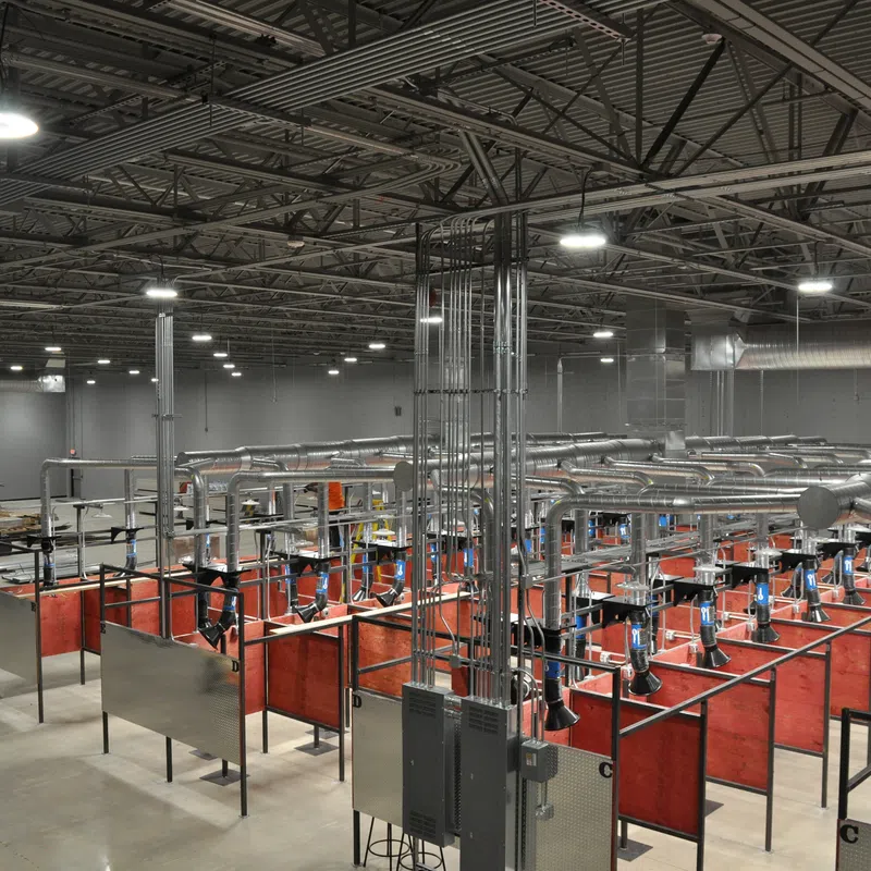 Interior view of a large industrial workshop with multiple welding stations and ventilation ducts under bright lighting