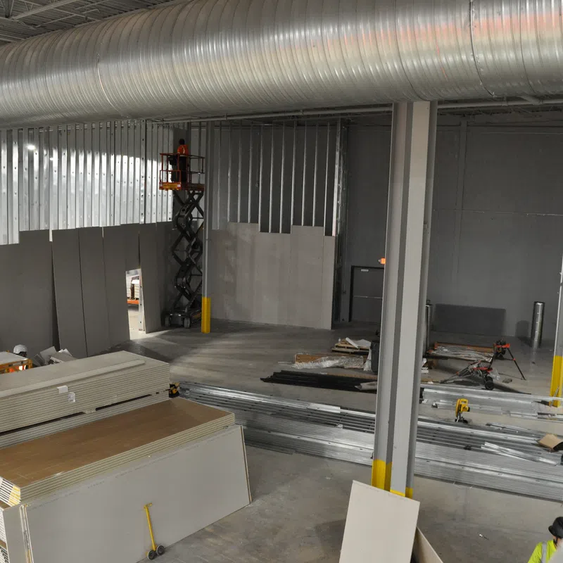 Interior view of a commercial building under construction with drywall stacks, metal framing, and ventilation ducts.