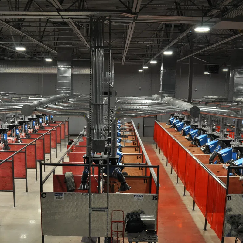 Industrial welding booths with ventilation systems in a large factory setting under bright ceiling lights
