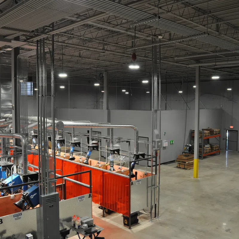 Modern industrial welding facility with multiple stations enclosed by red safety curtains and a yellow Komatsu forklift.