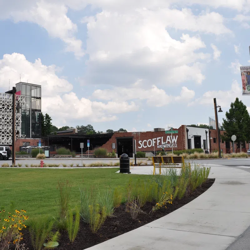 Scofflaw Brewing Co. building with a curved sidewalk, green lawn, flowers, and partly cloudy sky in the background.