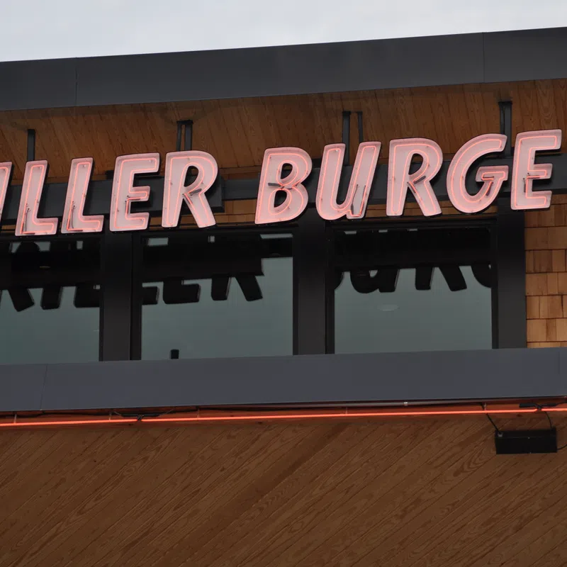 Killer Burgers neon sign mounted on wooden shingle wall above windows at burger restaurant.