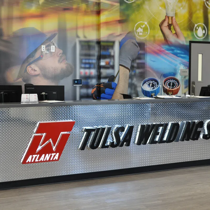 Reception desk with Tulsa Welding School logo and industrial-themed wall mural in modern training center.