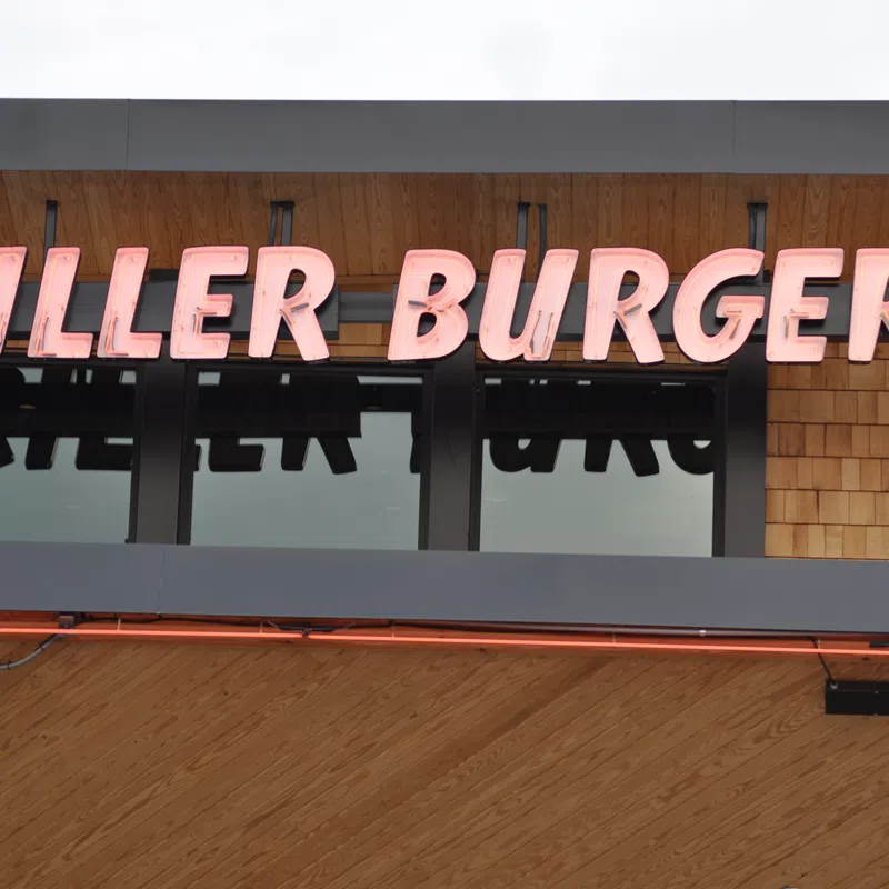 Bright pink neon sign reading Killer Burgers mounted on wooden exterior above windows.