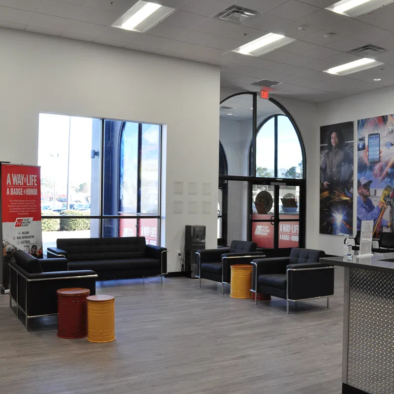 Modern office lounge with black sofas, colorful barrel stools, large windows, and vibrant wall art panels.