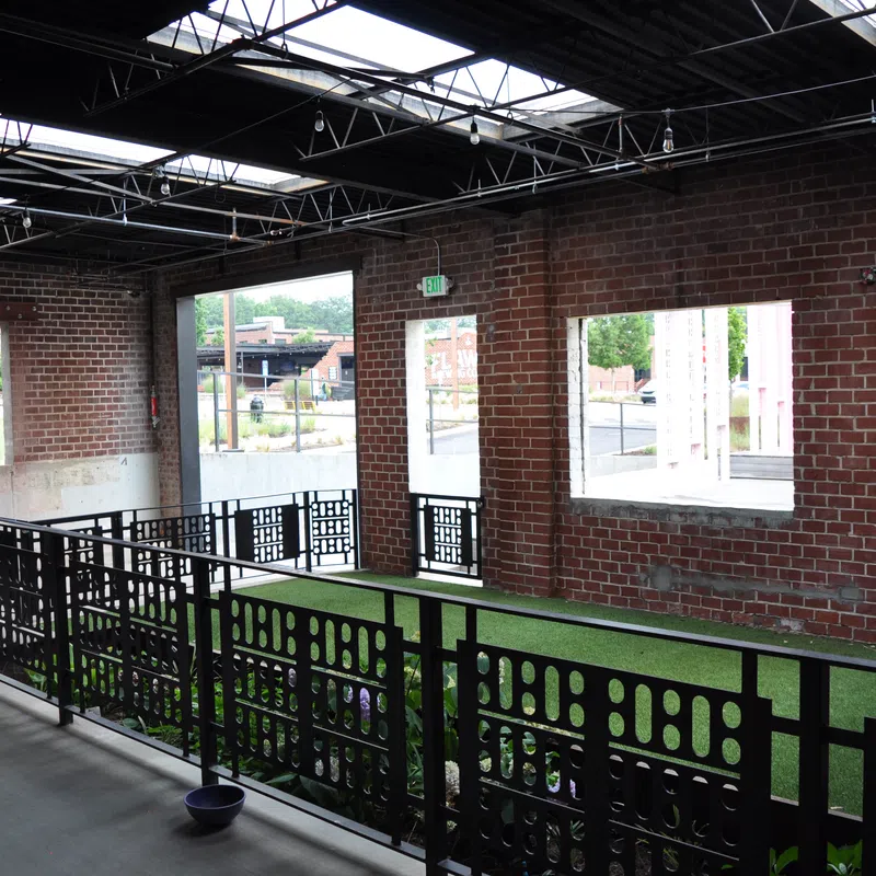 Indoor space with brick walls, large windows, black metal railings, and artificial grass flooring under steel roof beams.