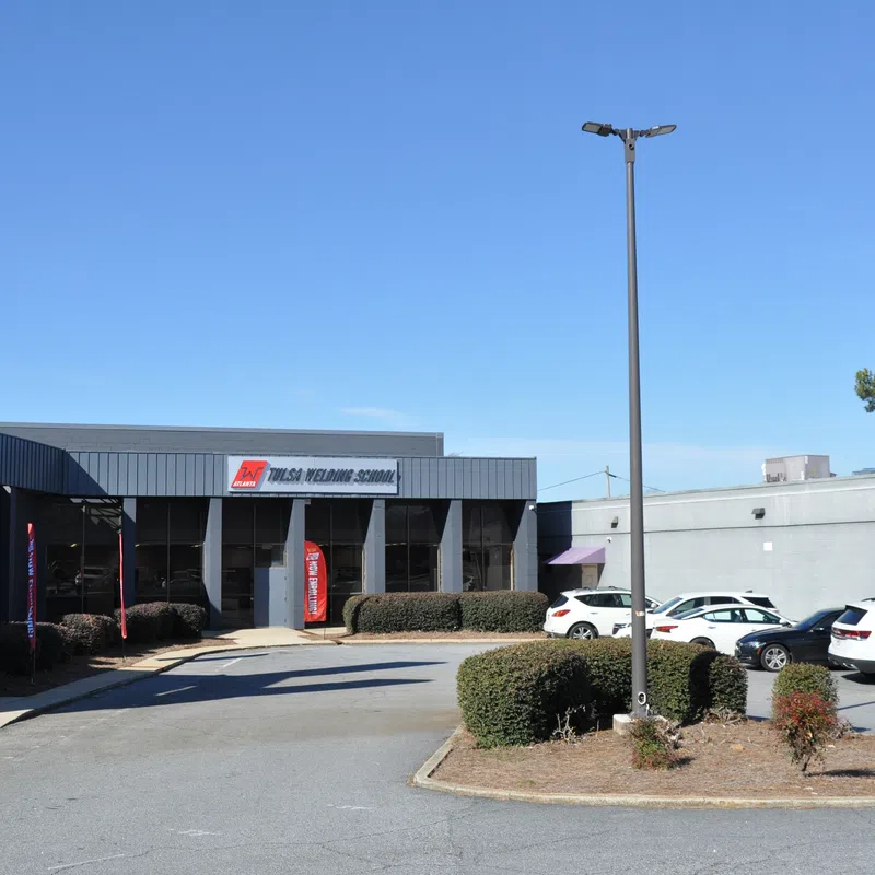 Exterior view of Tulsa Welding School building with parked cars under a clear blue sky.