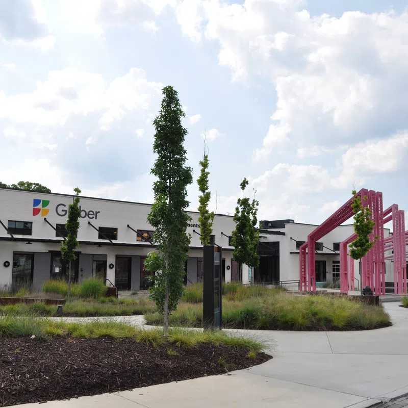 Modern office building with landscaped greenery and pink outdoor architectural installation under a cloudy sky