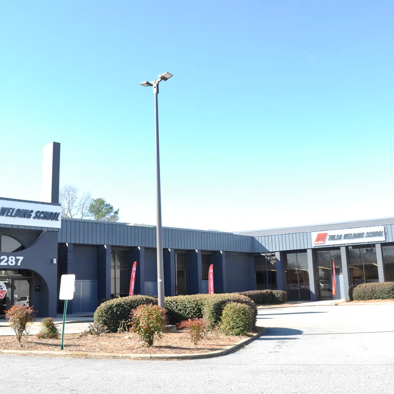 Front view of Tulsa Welding School building with signage, parking lot, and clear blue sky.