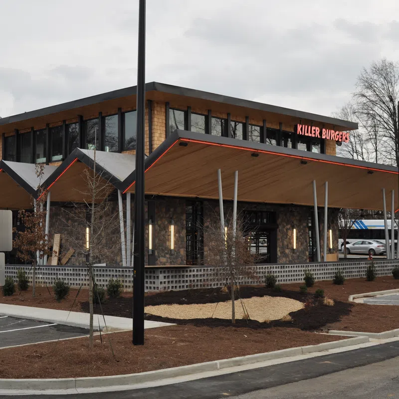 Modern Killer Burger restaurant with sharp angled roof, large windows, and parking lot on a cloudy day