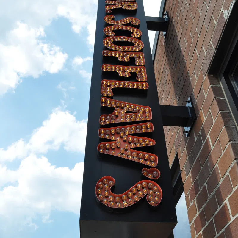 Upside-down vintage marquee sign with light bulbs on a brick building under a blue sky with clouds.