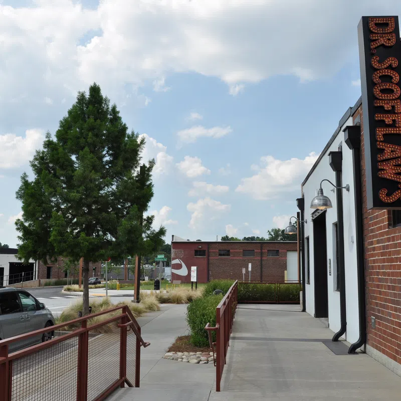 Outdoor sidewalk view of Dr. Scott Law's office with brick walls, trees, parked cars, and partly cloudy sky.