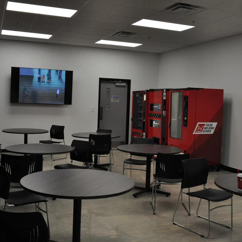 Break room with round tables, black chairs, red vending machines, and a TV mounted on the wall.