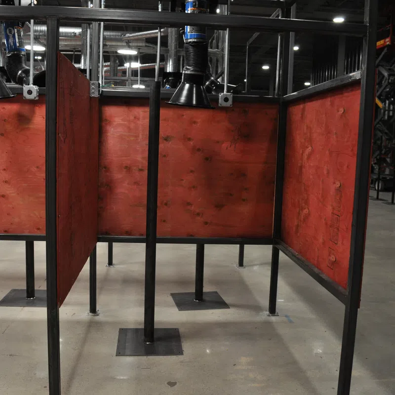 Indoor industrial welding booths with red wooden panels and ventilation ducts in factory setting.