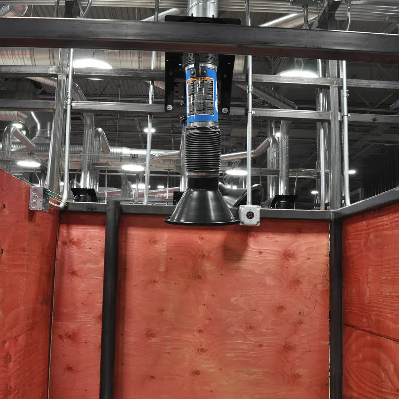 Industrial workspace with red wooden walls and overhead ventilation and duct system in a factory setting.