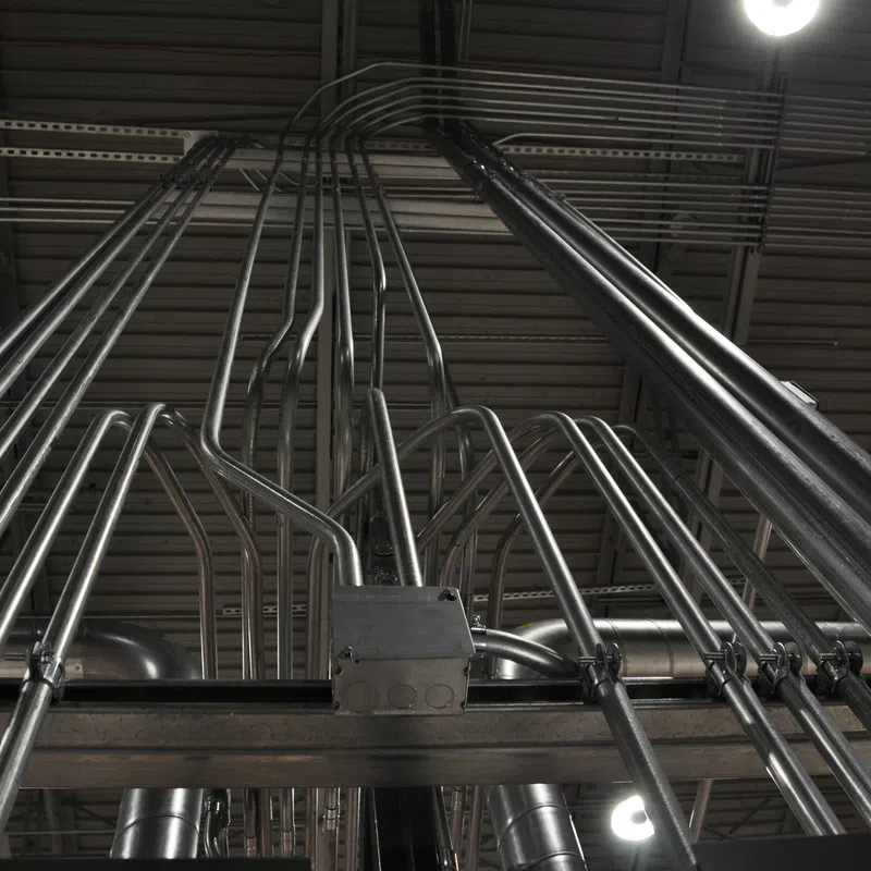 Low angle view of shiny metal electrical conduits running vertically and horizontally across an industrial ceiling.