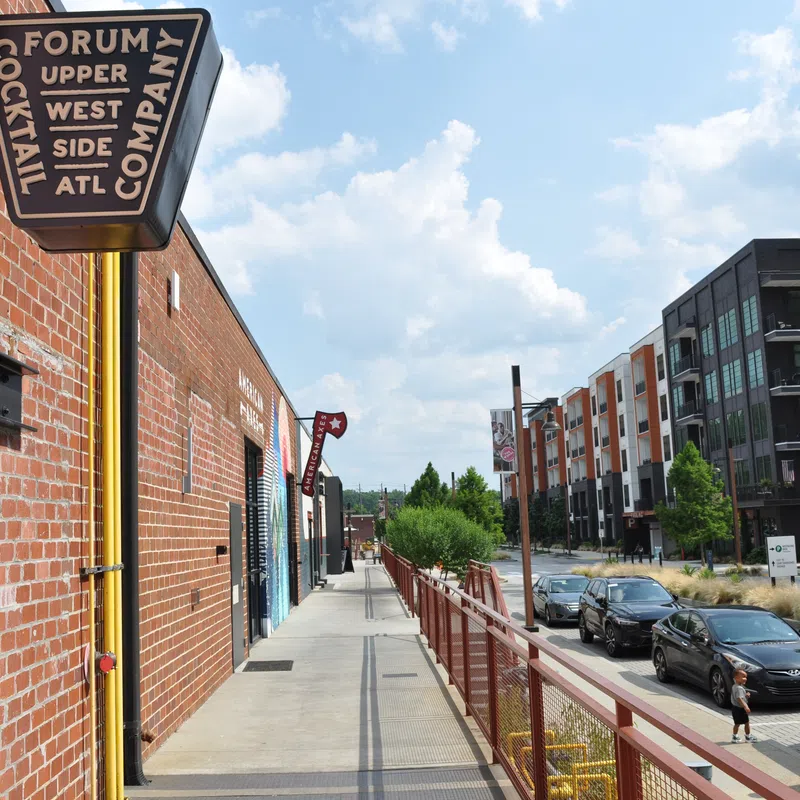 Sidewalk view of Forum Cocktail Company sign on brick building with street and modern apartments in Atlanta