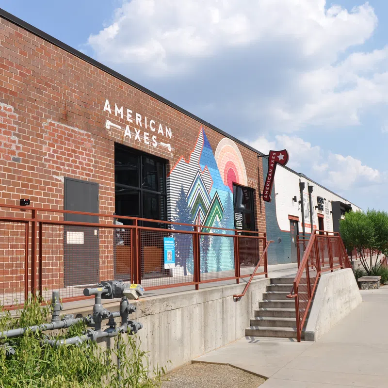 Exterior view of American Axes building with brick wall, colorful mural, and sidewalk under blue sky