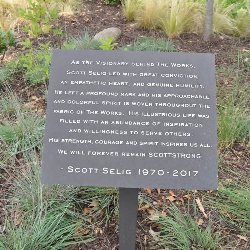 Memorial plaque honoring Scott Selig's vision, empathy, and inspiring life surrounded by plants and grass.