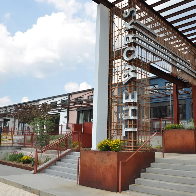 Exterior of a modern building with rust-colored metal structure and stairs under a cloudy sky.