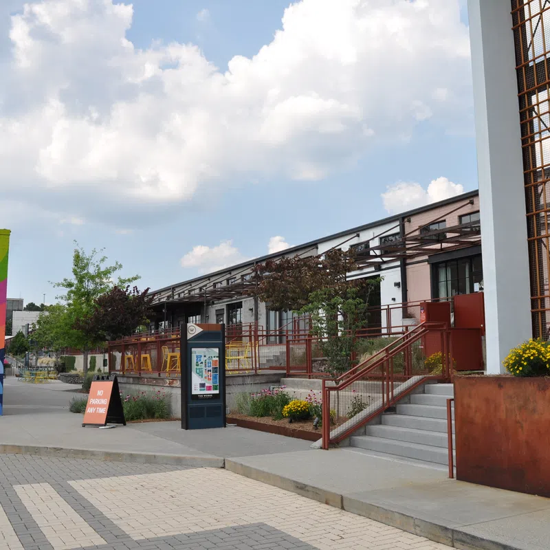 Outdoor urban plaza with colorful mural, modern buildings, stairway, and clear sky with scattered clouds.