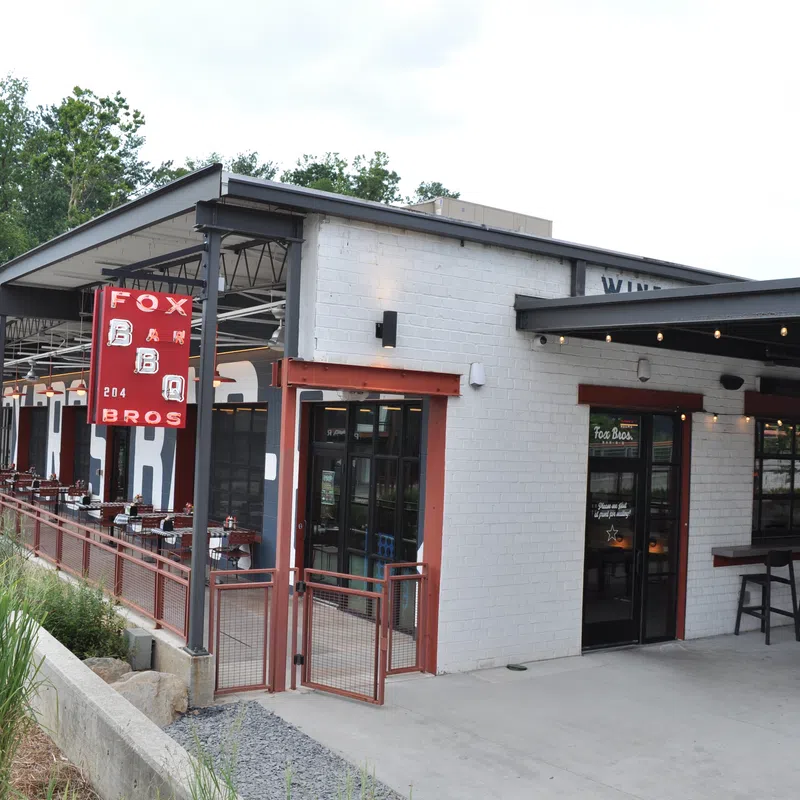 Exterior view of Fox Bros BBQ restaurant with outdoor seating and red signage on a bright day.
