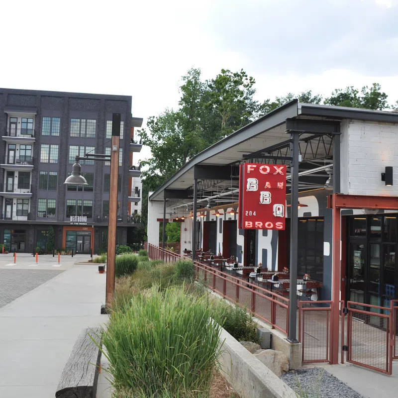 Modern BBQ restaurant with outdoor seating and urban apartment buildings in the background on a bright day.