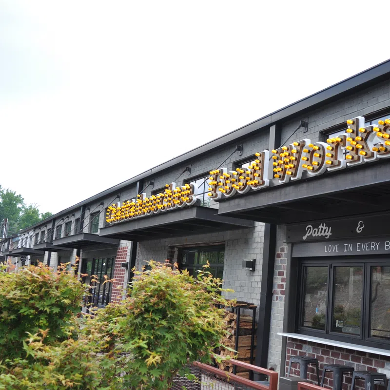 Exterior view of a brick food market with illuminated Food Works sign and greenery in front on a clear day