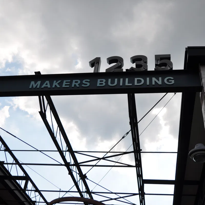 Structural metal beam with Makers Building sign and 1235 number against cloudy sky background.