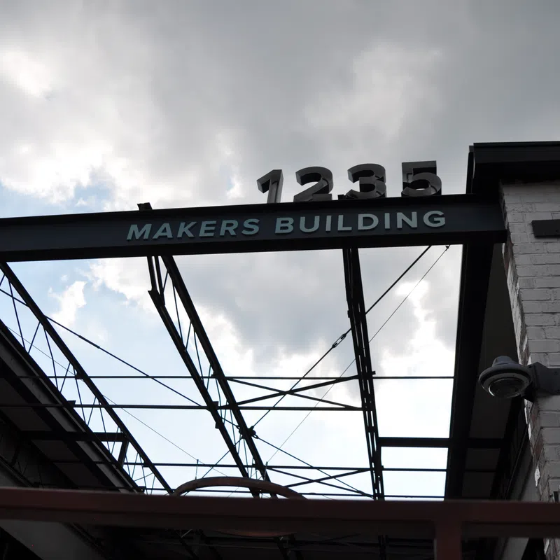 View of the Makers Building entrance with metal framework and address number 1235 against a cloudy sky.