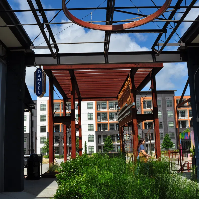 Outdoor modern urban area with metal structures, greenery, and a person walking near apartment buildings on a sunny day