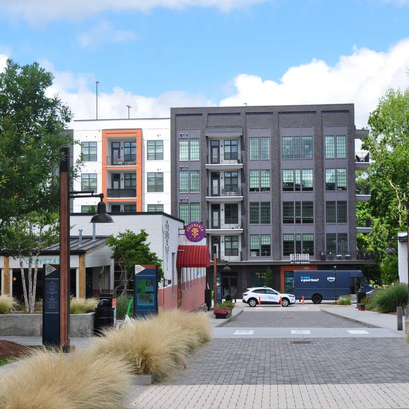 Modern urban plaza with shops, greenery, paved walkway, and multi-story residential buildings under blue sky