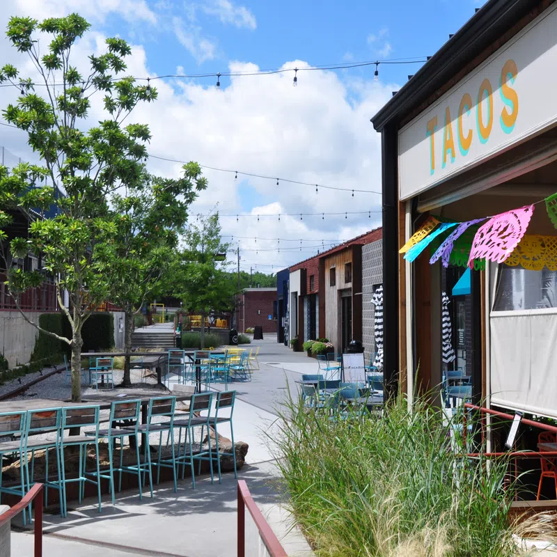Outdoor seating area of a taco restaurant with colorful decorations and string lights under a bright sky.