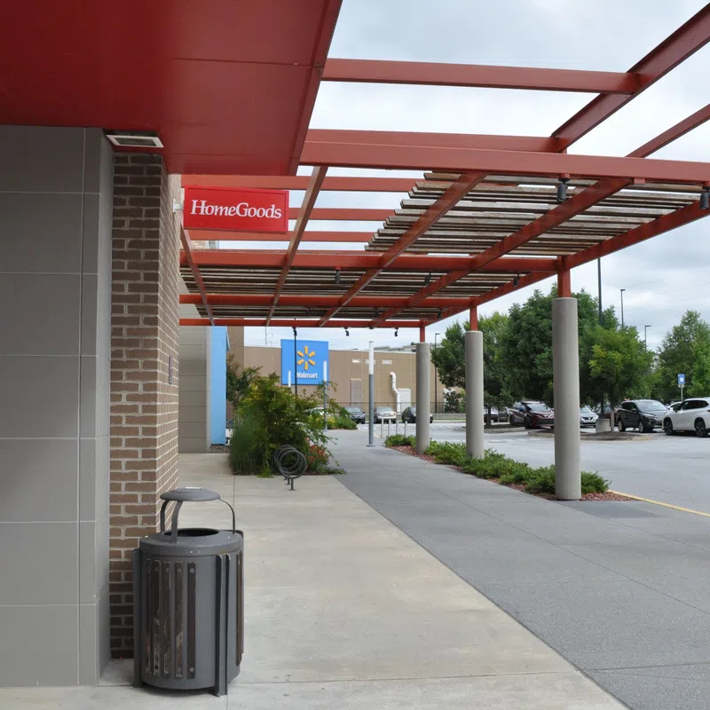 Outdoor shopping plaza with HomeGoods and Walmart stores under red metal canopy and parking lot on a cloudy day