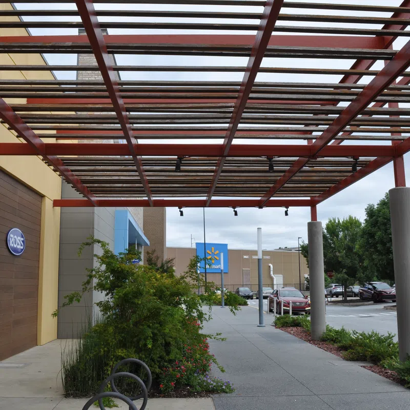 Outdoor shopping area with Ross and Walmart stores, covered walkway, plants, and parked cars on a cloudy day