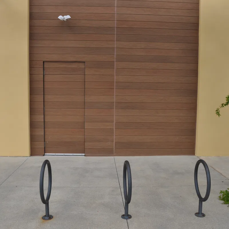 Empty bike racks in front of a modern wooden and yellow building wall with a concealed door and greenery.
