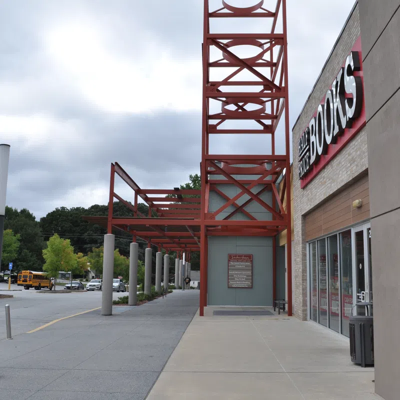 Exterior view of a bookstore entrance with red metal framework and a cloudy sky overhead.
