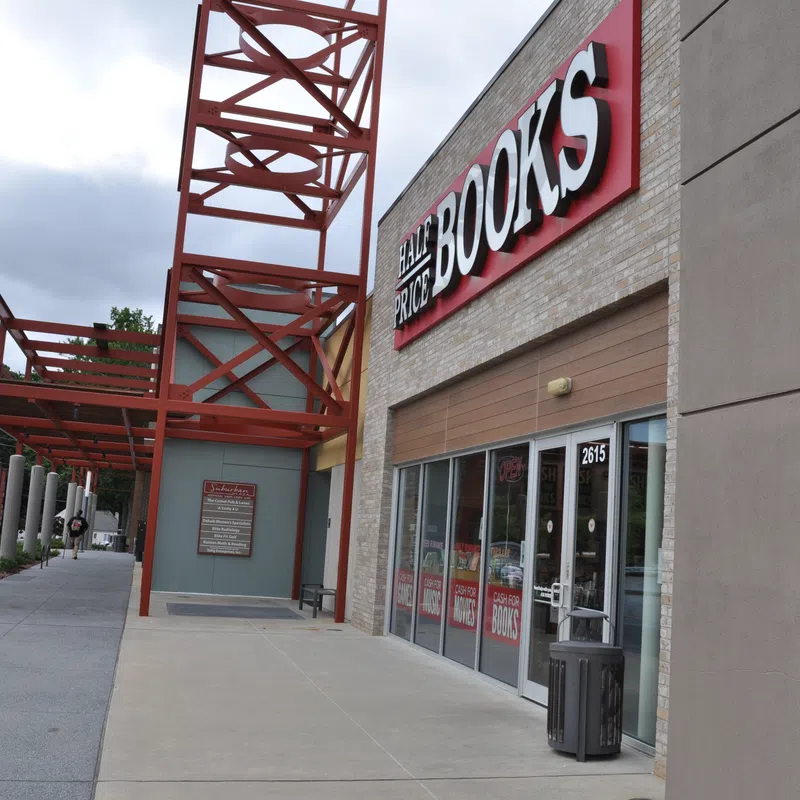 Exterior view of Half Price Books store with red metal framework and clear sidewalk under cloudy sky.