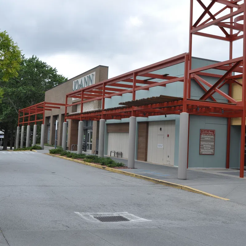 Exterior view of a Joann fabric and craft store with red metal awnings and a tree-lined parking area.