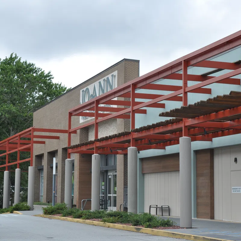 Exterior view of a Joann fabric and craft store with red metal framework and surrounding greenery